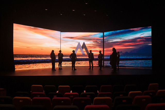 LED screen installed on a stage where people are seen admiring the sunset in a coastal area